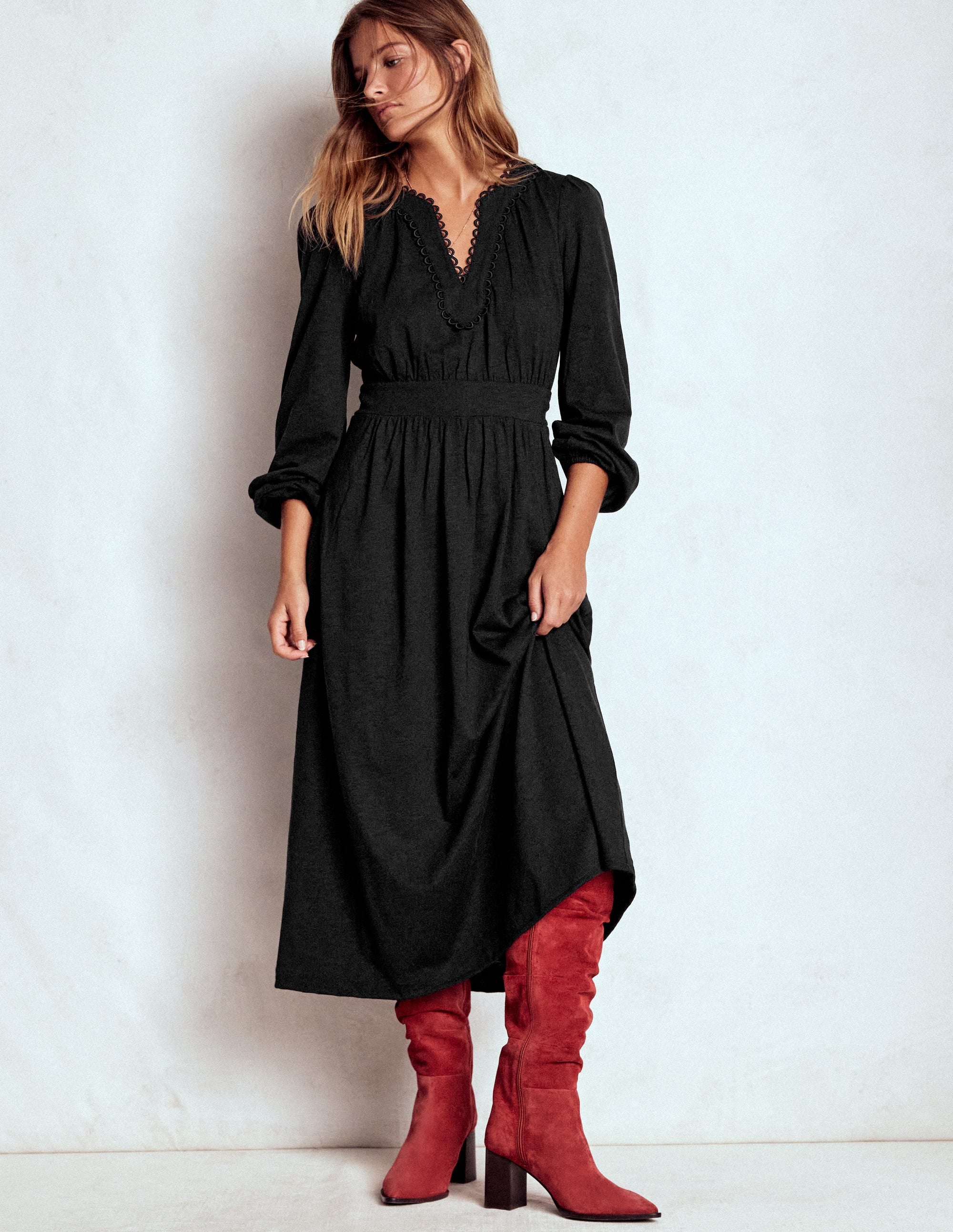 A woman wearing a black midi dress with blouson sleeves, a picot trim on the V-neckline, and a fitted waist.