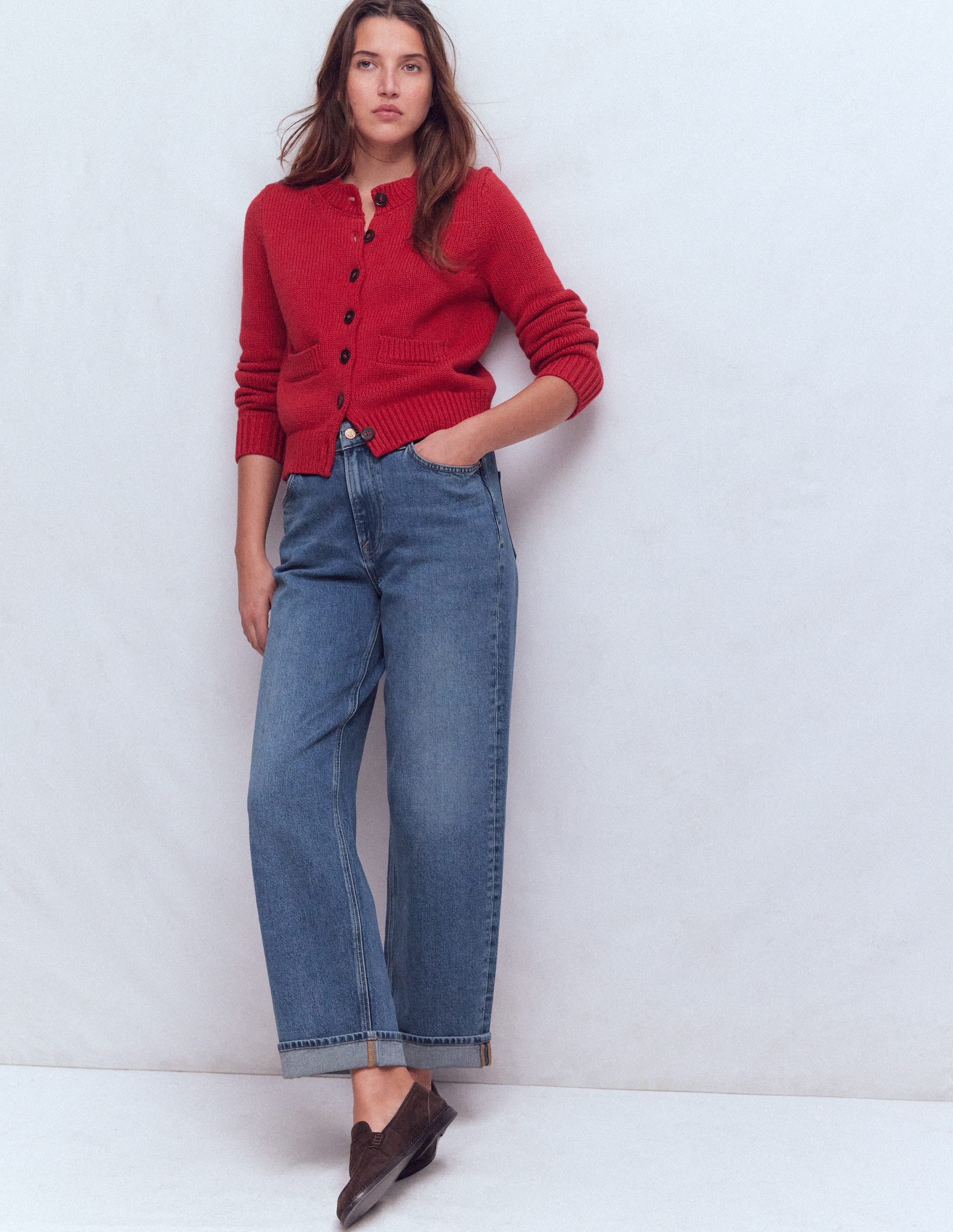 A woman wearing blue jeans with a mid-rise waist, wide straight legs, and turn-up cuffs, paired with a red cardigan.
