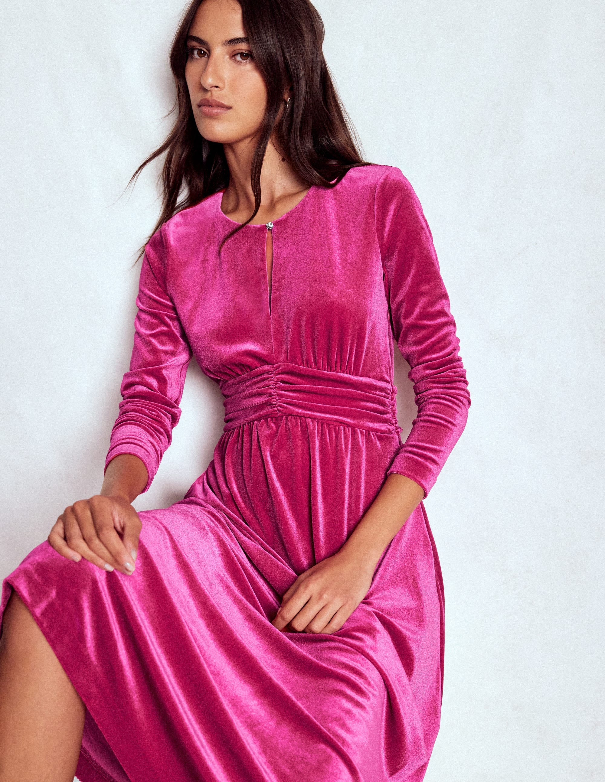 A woman wearing a vibrant pink velvet midi dress with long sleeves and a ruched waistband.