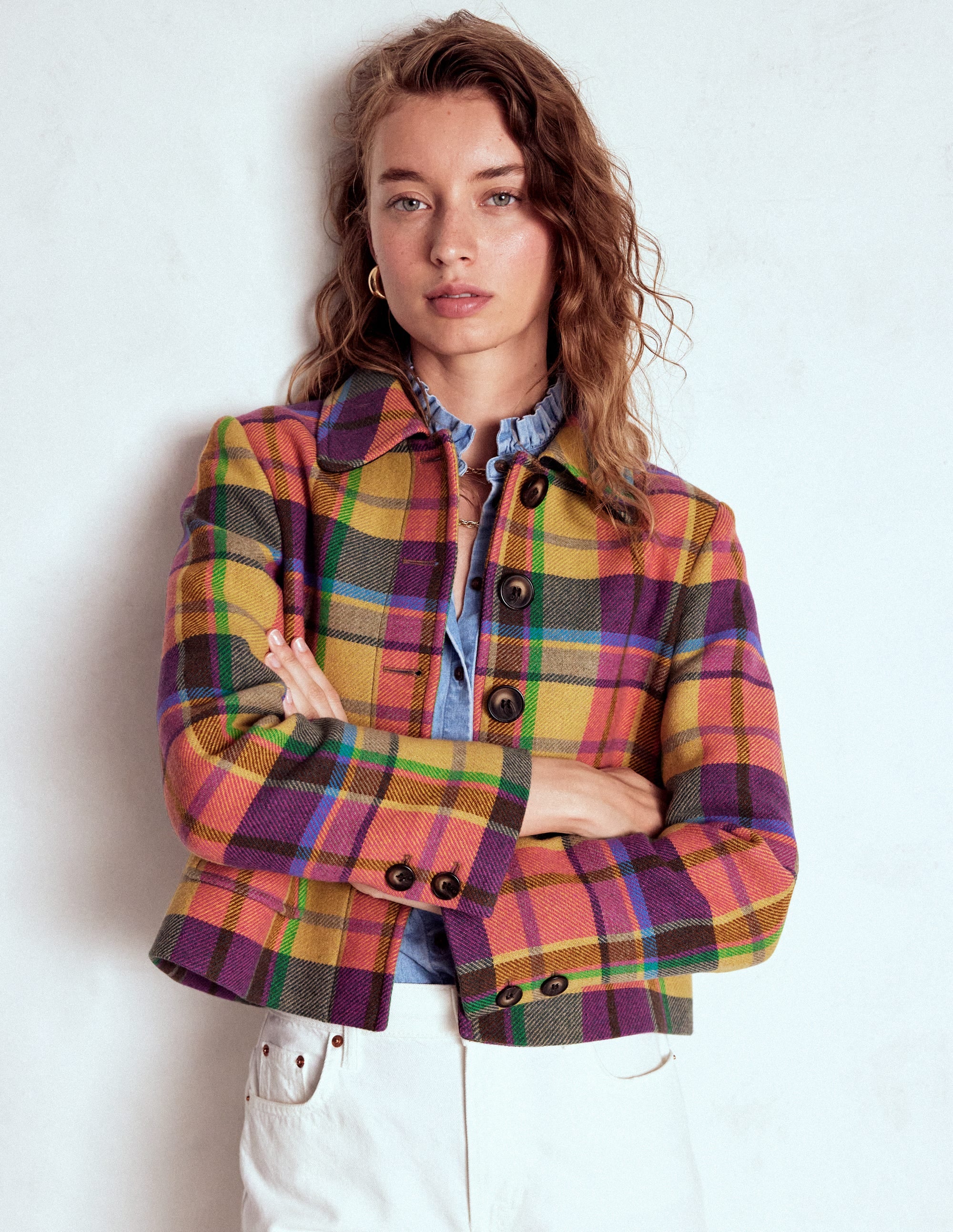 A woman wearing a multicolour check wool jacket with front pockets and a back box pleat, styled with a blue ruffled shirt underneath.