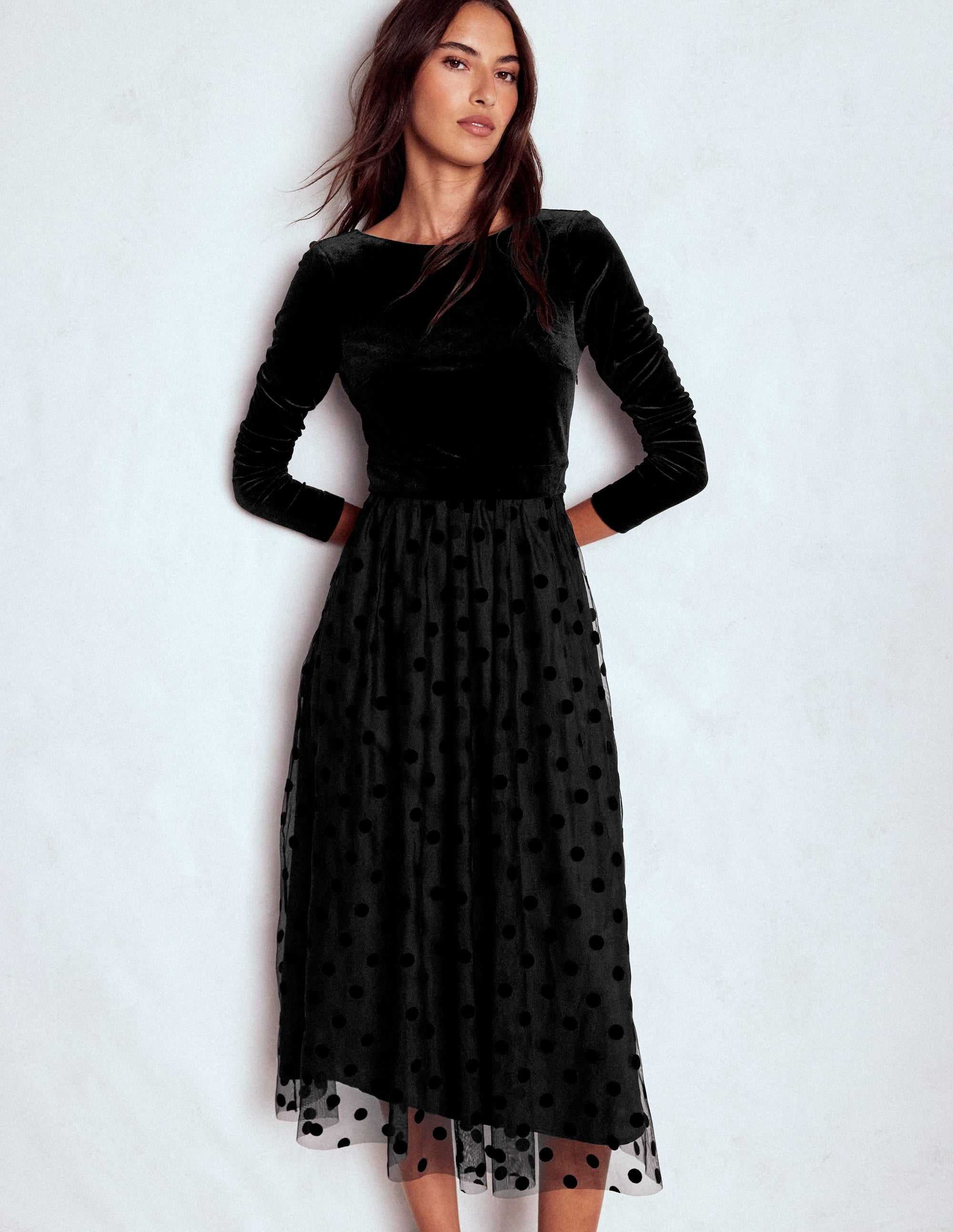 A woman wearing a black velvet bodice jersey dress with long sleeves, scoop back, and a polka dot tulle skirt.