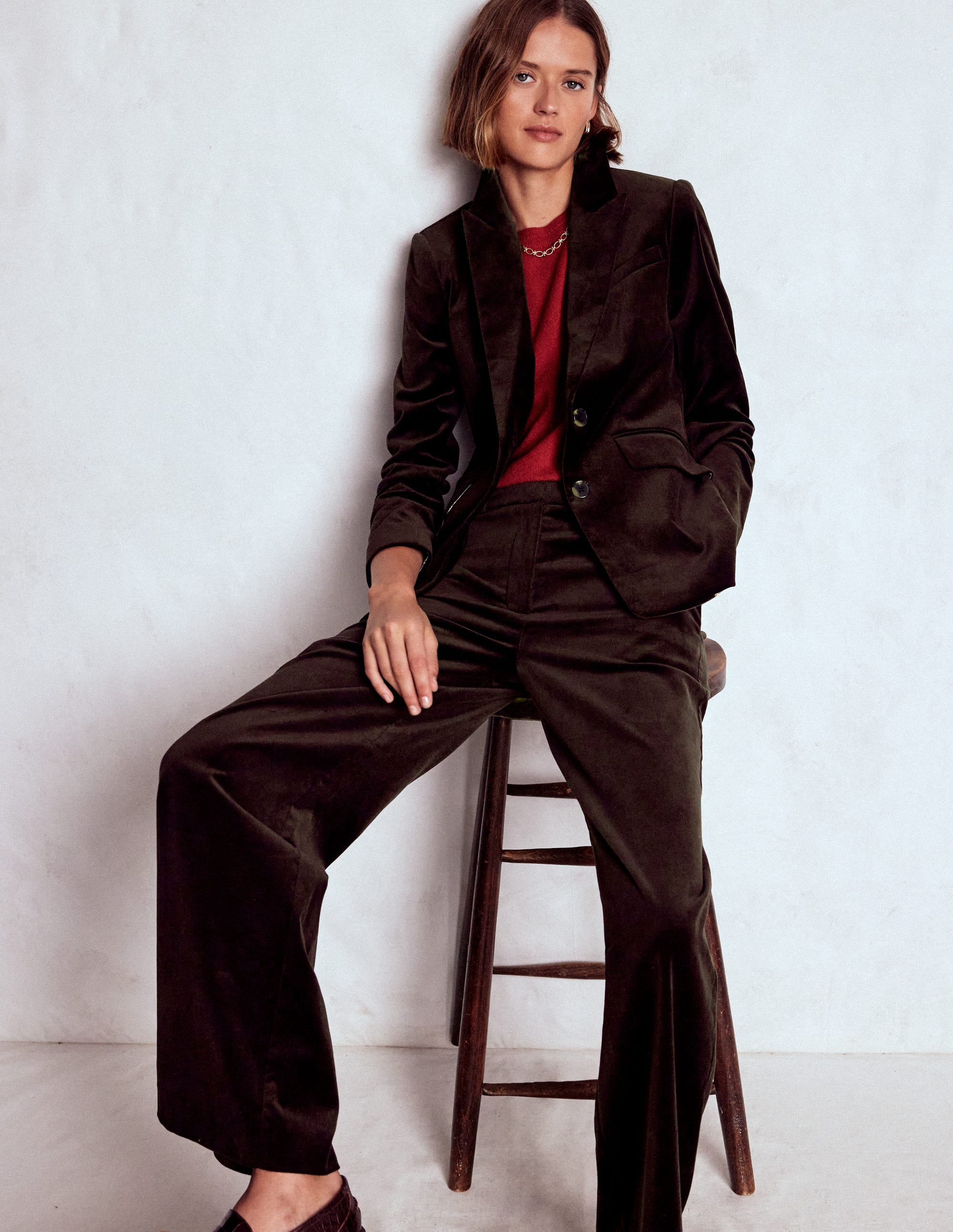 A woman wearing a dark brown velvet blazer with a structured fit, button closure, and a notched collar, paired with matching trousers and a red top.