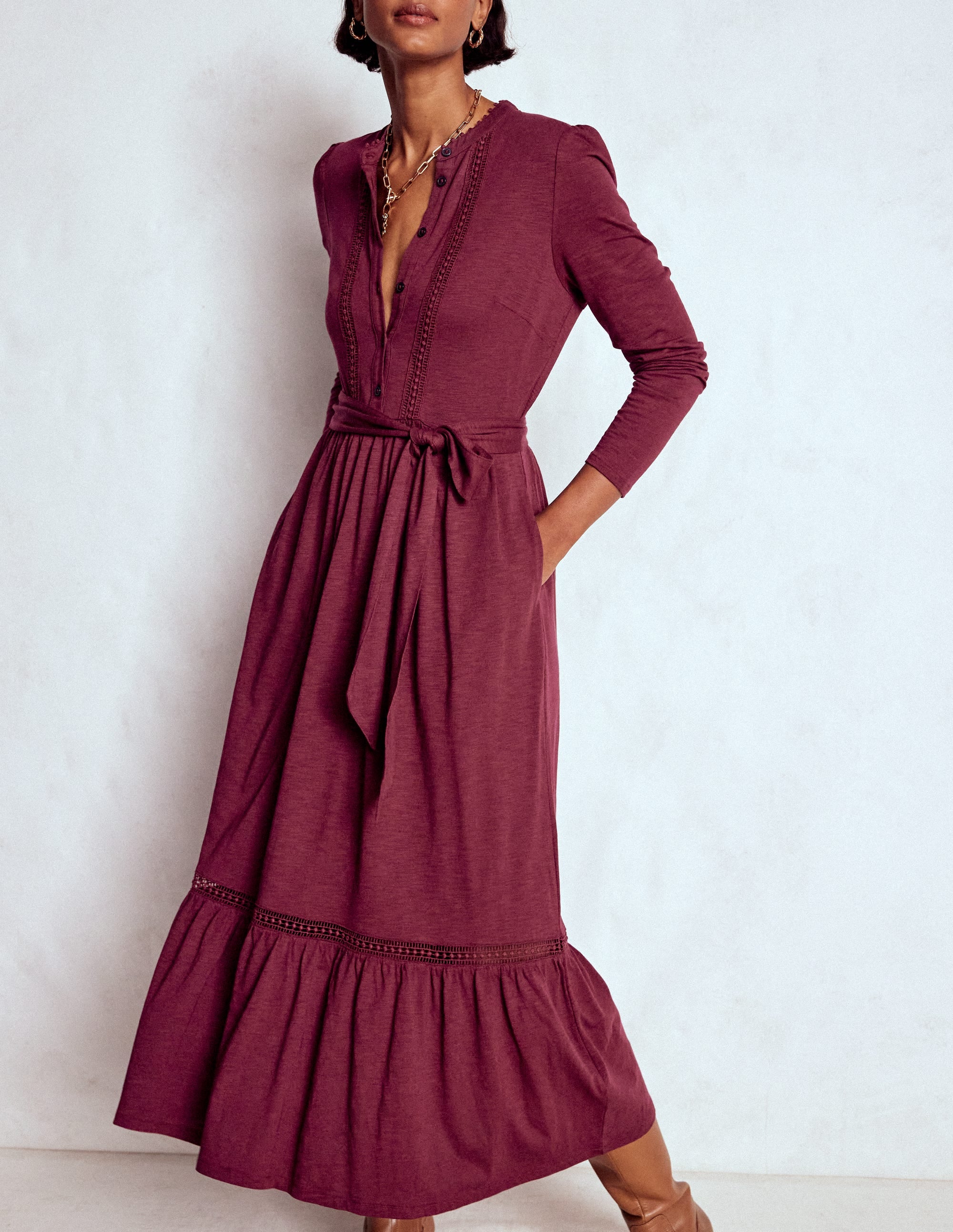 A woman wearing a Deep Wisteria colored maxi shirt dress with a fabric belt, tiered skirt, and side pockets.