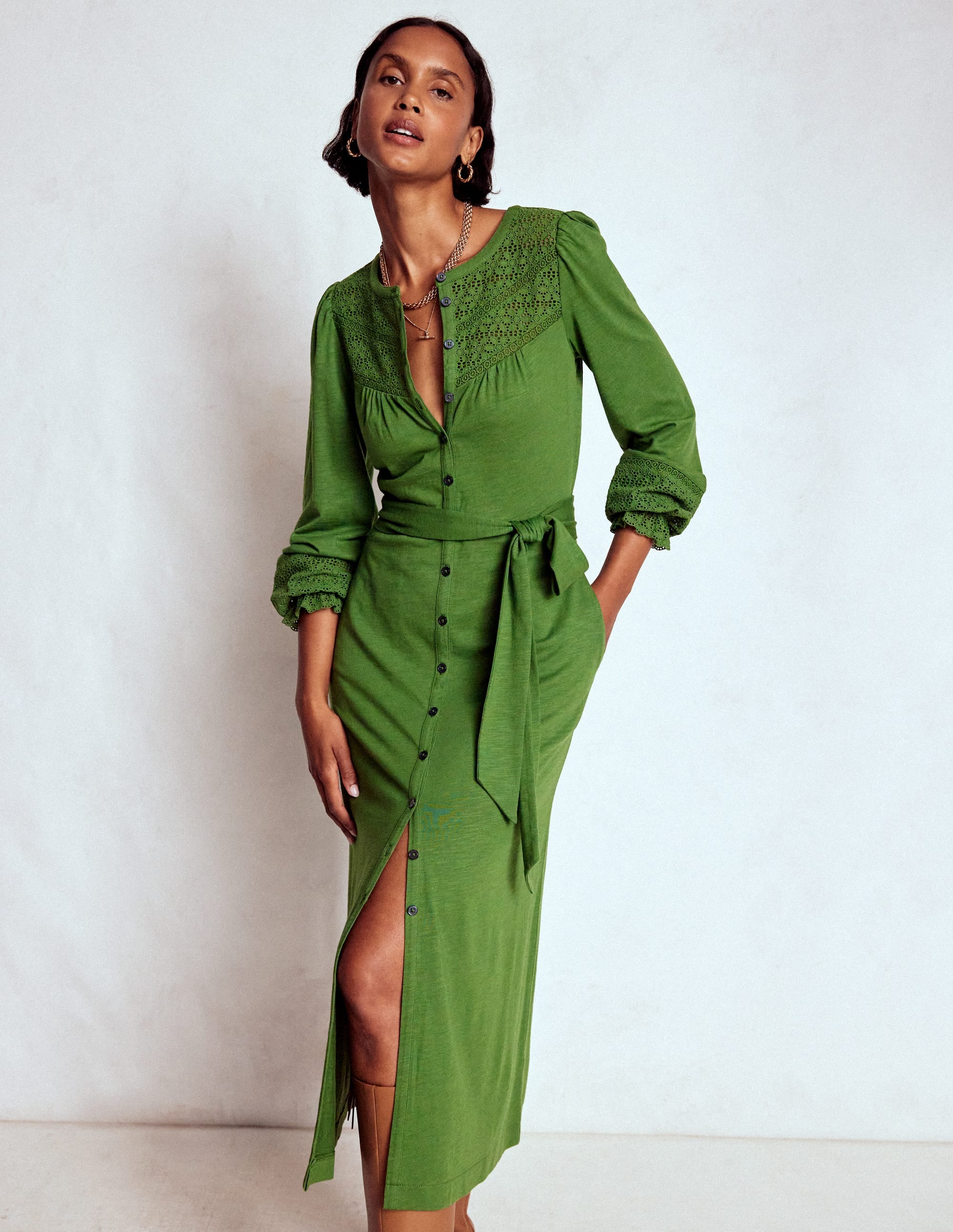 A woman wearing a Promenade Green broderie jersey dress with long sleeves, a button-down front, and a self-fabric belt, standing against a plain background.