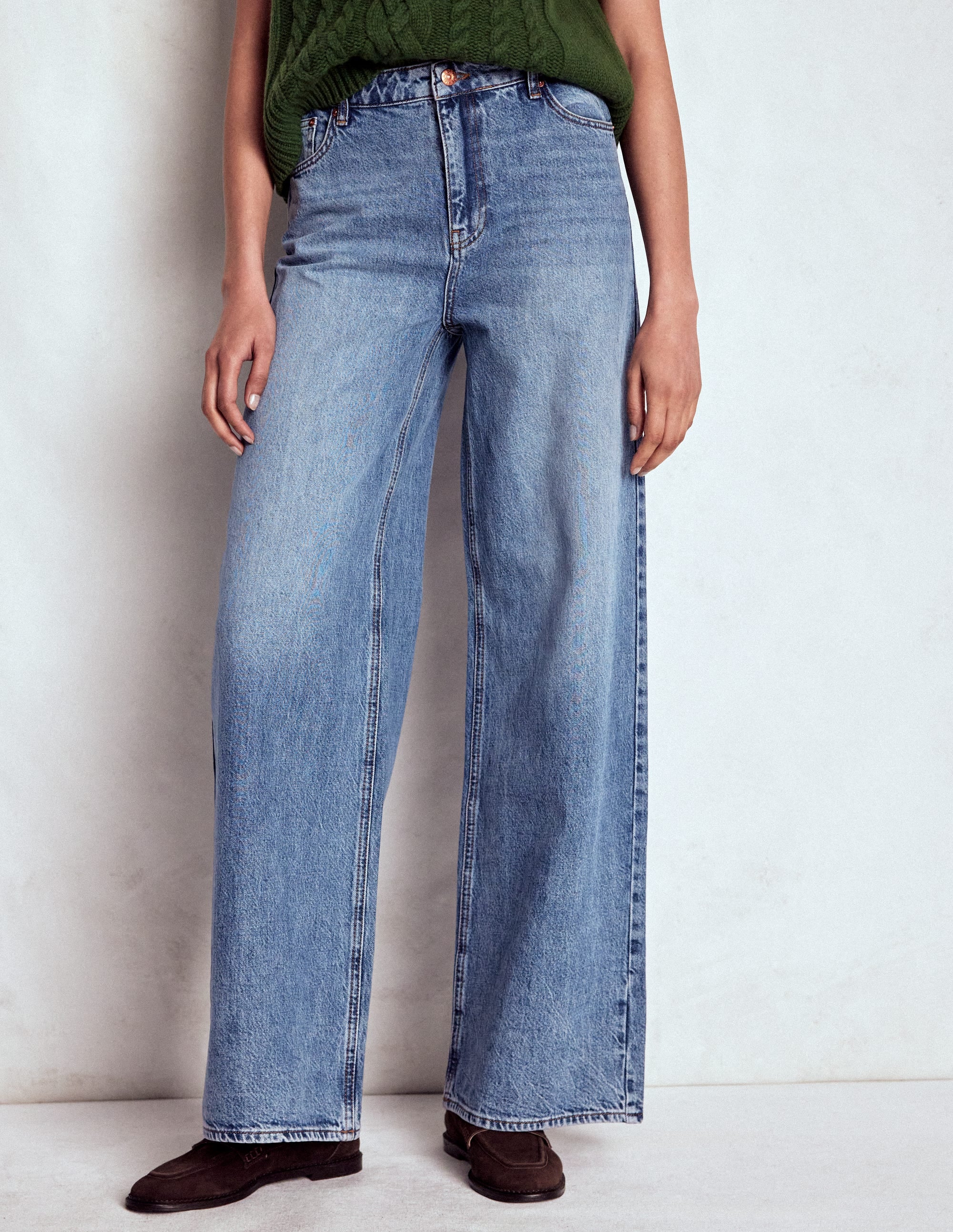 A pair of light blue relaxed wide-leg jeans with a vintage wash, styled with a five-pocket design, sitting at the waist, with a zip fly and button, and styled with a green top.