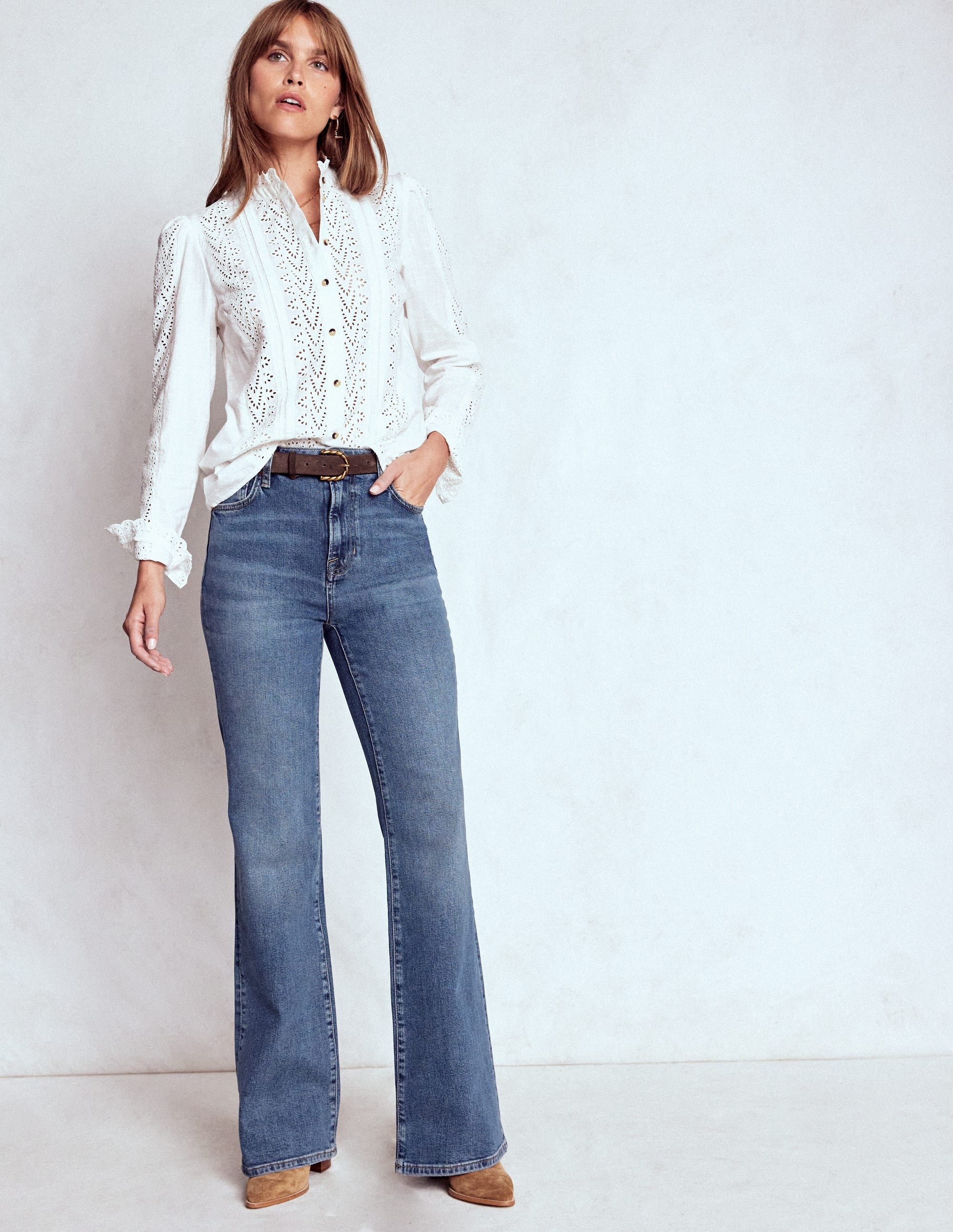 A woman wearing blue high-rise fitted flare jeans with a vintage wash, paired with a white blouse.