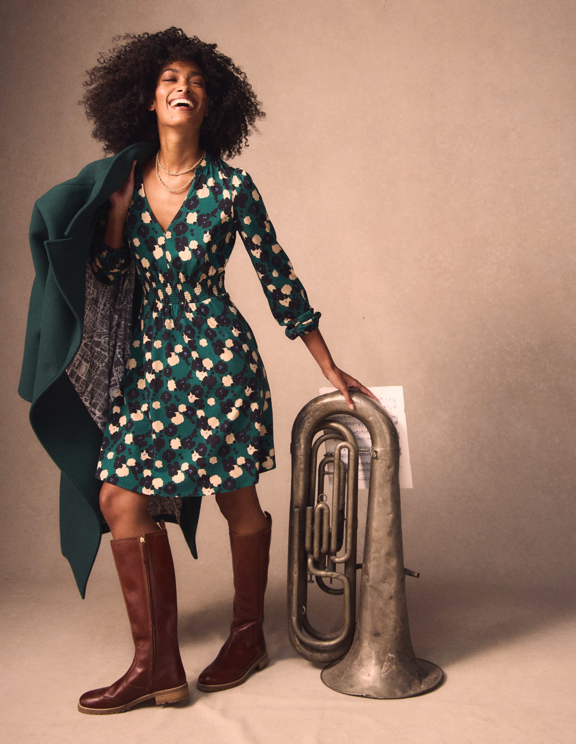A woman wearing a knee-length, floral patterned jersey dress in emerald night color, with long sleeves and a V-neckline, standing next to a musical instrument.