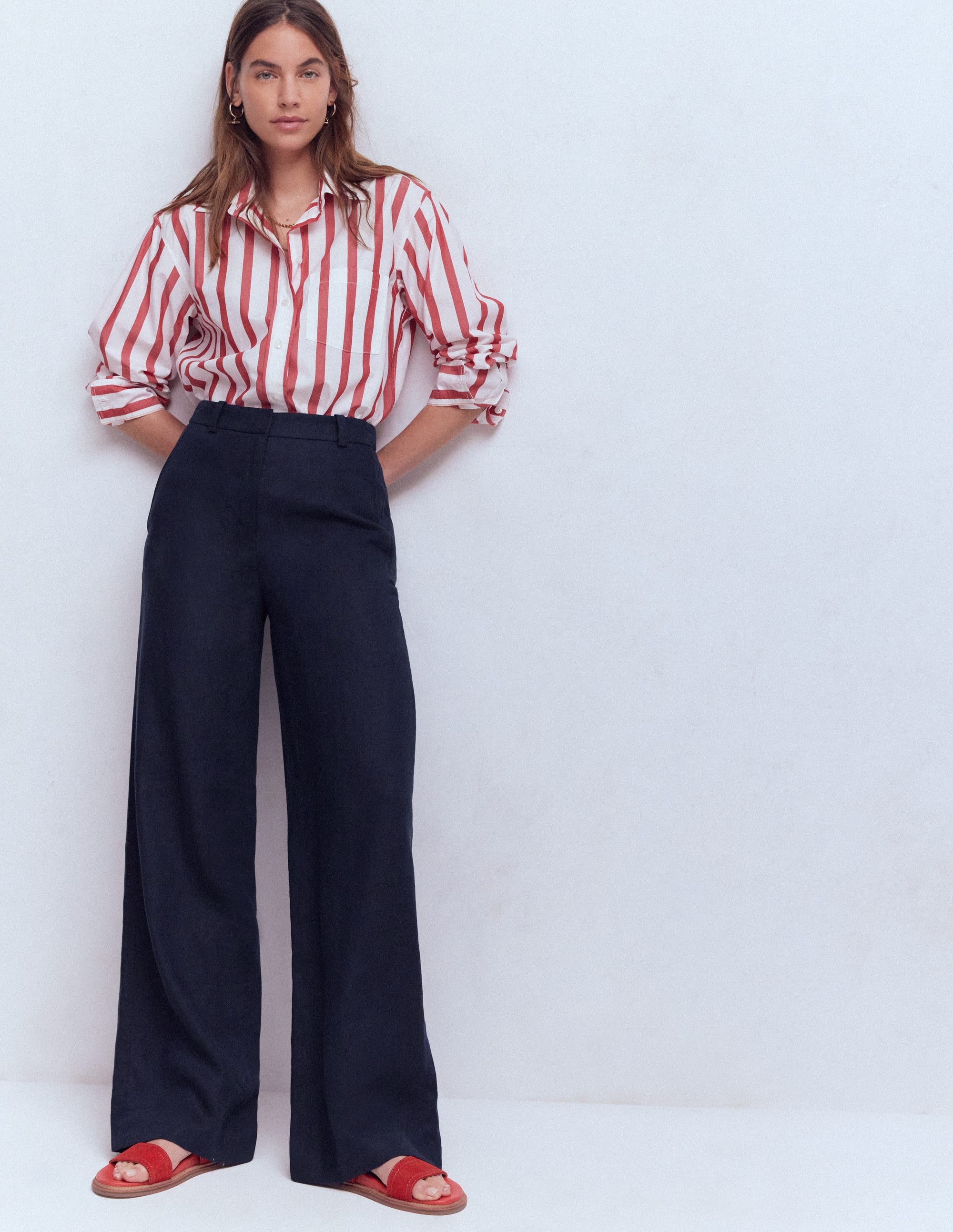 A woman wearing navy linen trousers with a wide-leg cut, paired with a red and white striped shirt, standing against a plain background.