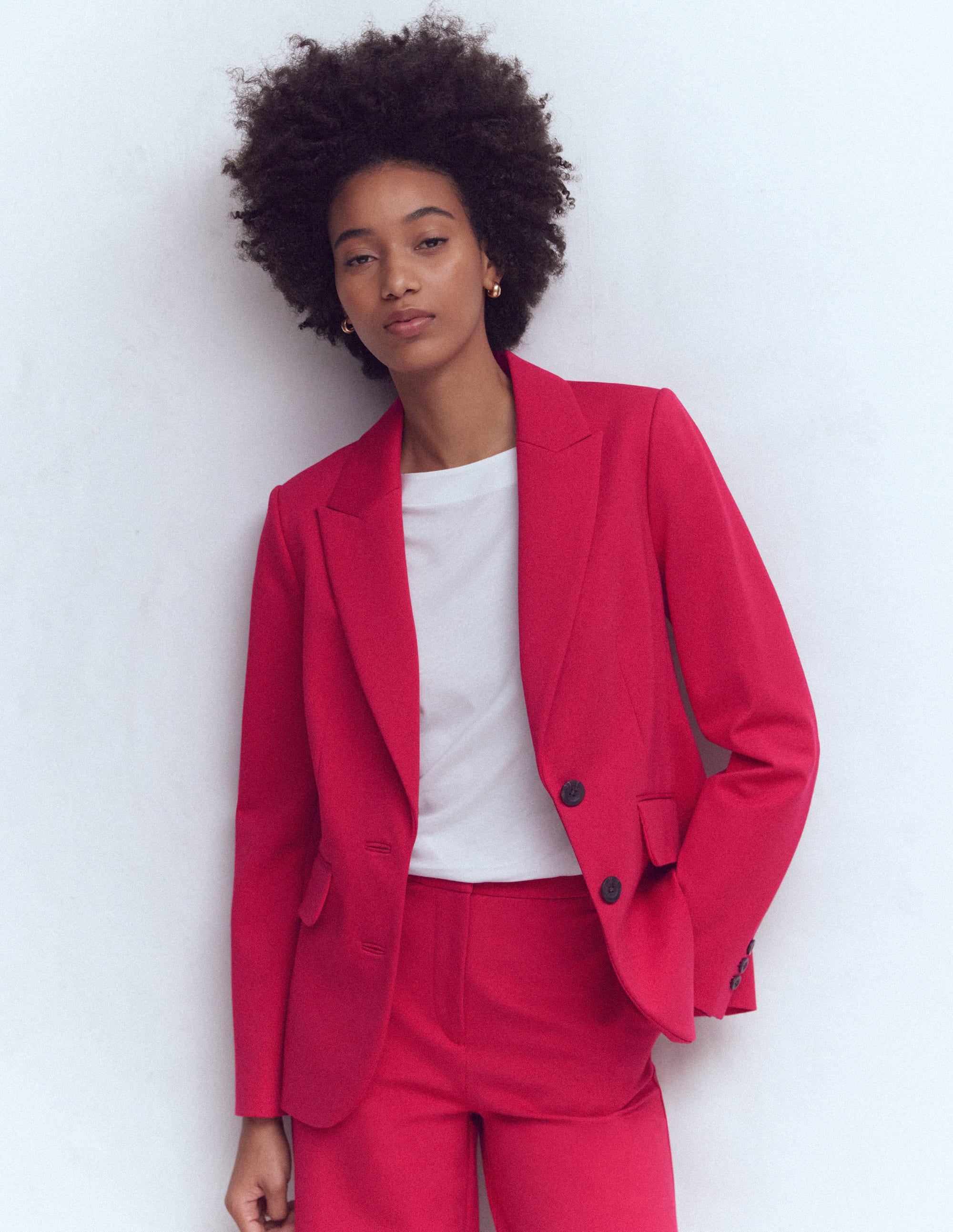 A woman wearing a bright red blazer with a lapel collar, front buttons, and functional pockets, paired with matching red trousers.