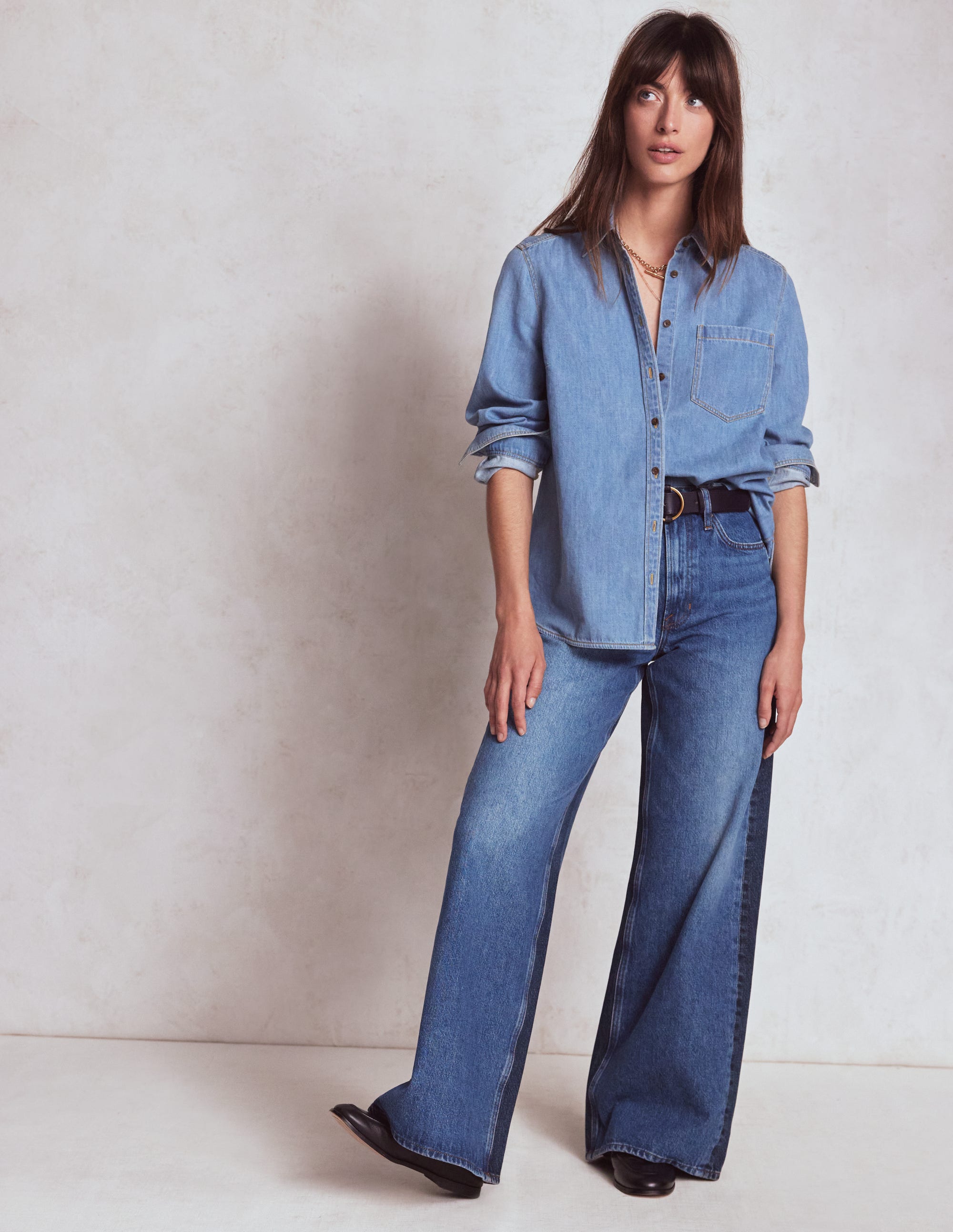 A woman wearing light blue high-rise wide-leg jeans with a button and zip fly, five pockets, and a maxi length, paired with a denim shirt.